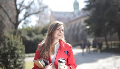 delighted female student with takeaway coffee and books in campus