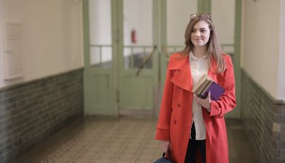 smart female student with books and backpack in university hallway