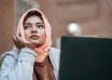 muslim female student daydreaming while sitting with laptop near city building