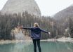 woman with arms outstretched standing on coast of lake